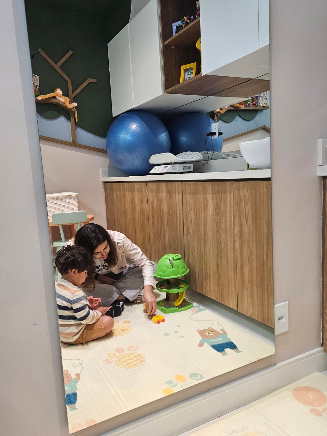 Sala de atendimento com tapete infantil e brinquedos, Alice brincando com uma criança